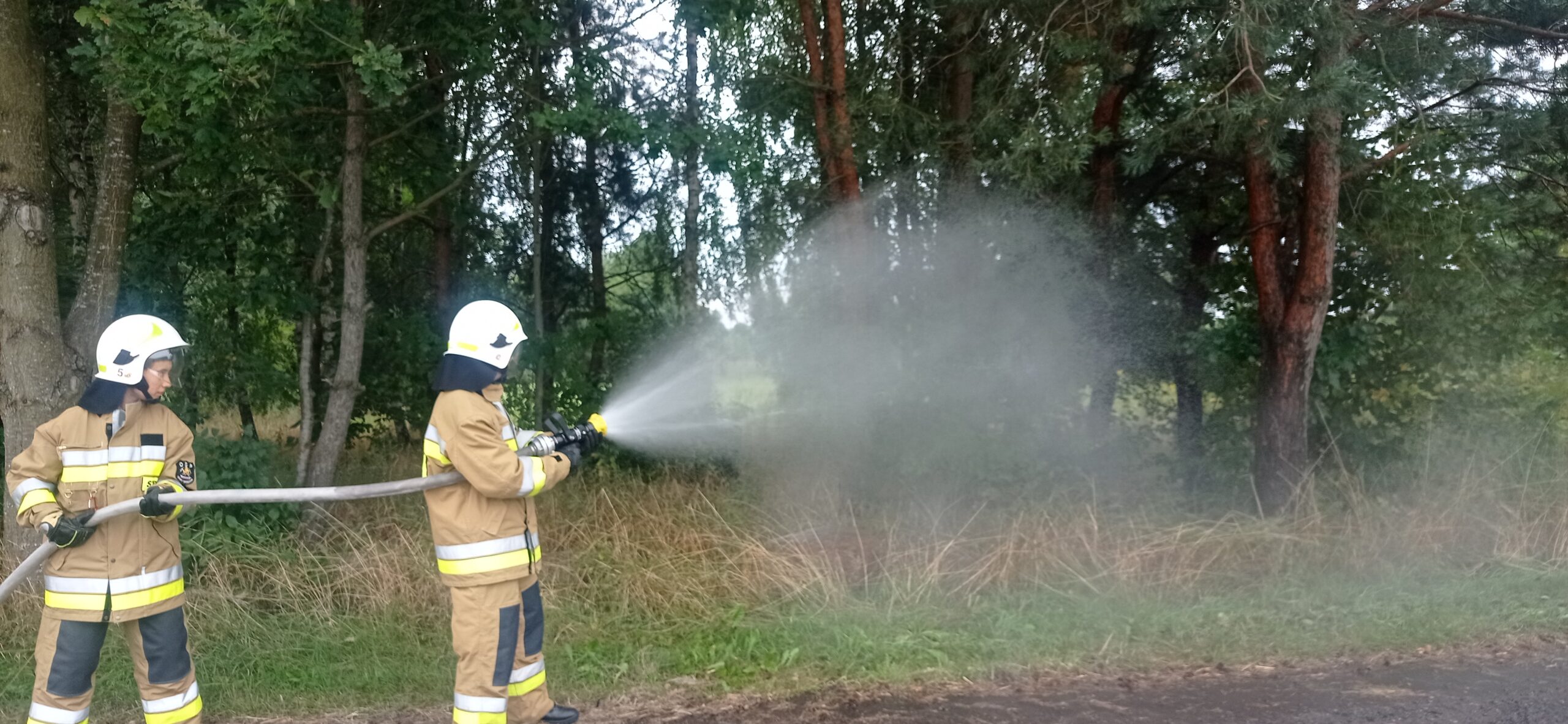 Dwóch strażaków ćwiczy podawanie prądów gaśniczych wody.