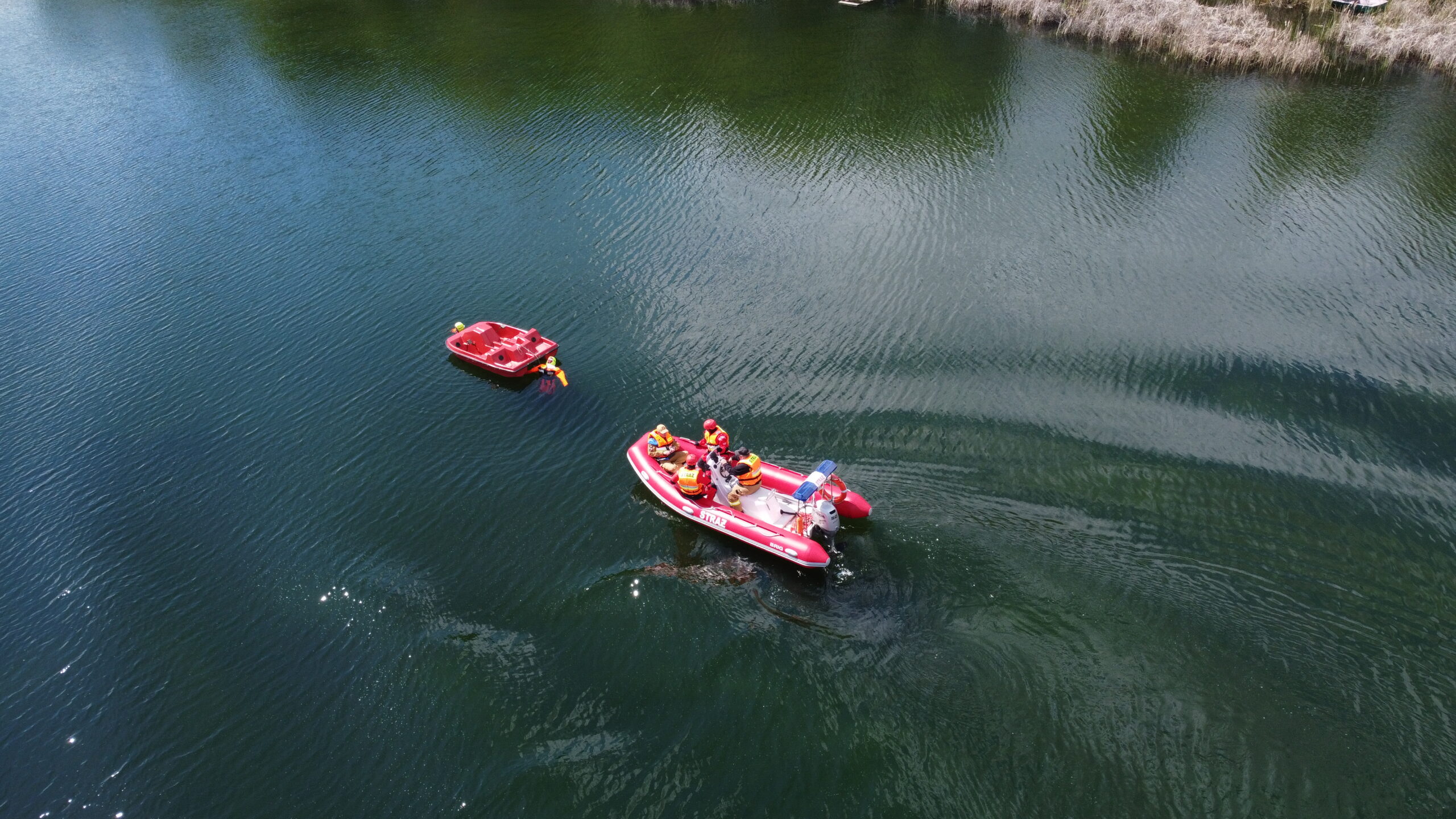 Ponton Straży Pożarnej podpływa do rowerka wodnego i pozorowanych poszkodowanych. Zdjęcie zrobione z drona