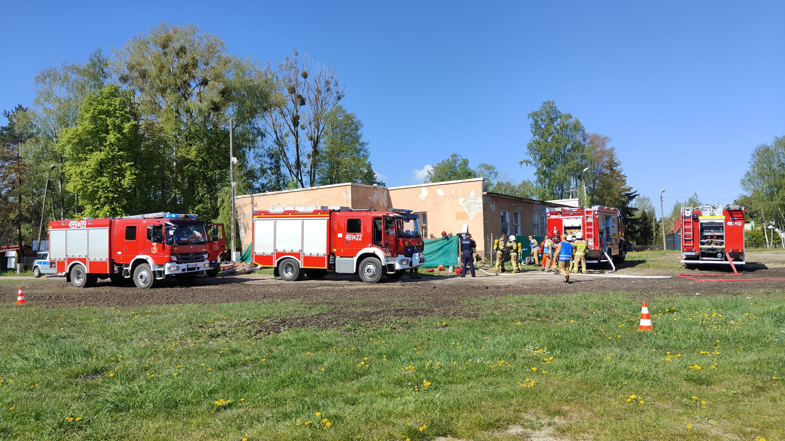 Pozorowany pożar budynku. W ćwiczeniu biorą udział cztery pojazdy pożarnicze, Zespół Ratownictwa Medycznego i Policja. Strażacy rozwinęli linie gaśnicze prowadzące do wnętrza budynku.