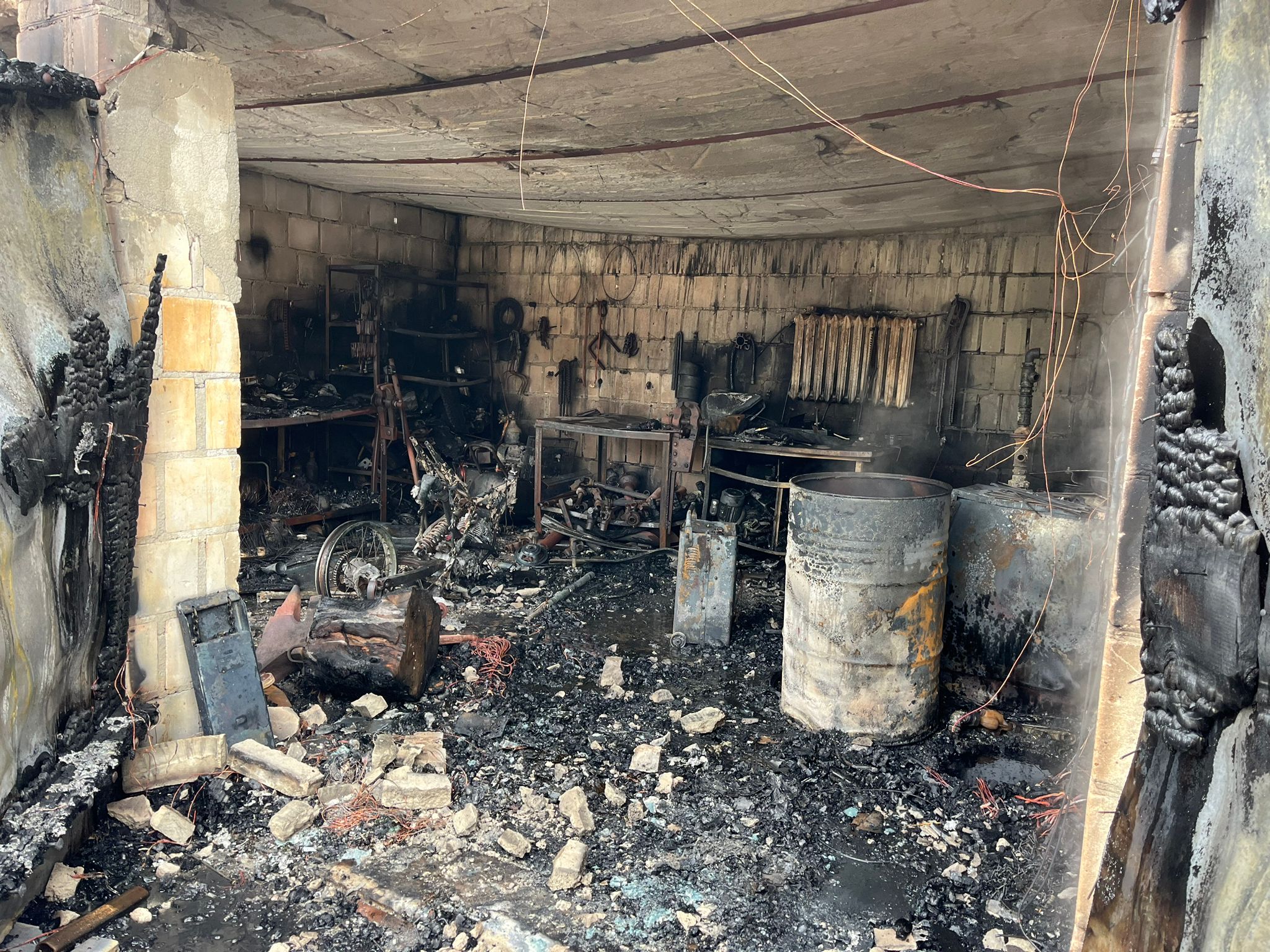 Zdjęcie przedstawia spaloną część garażową budynku, spalony sprzęt i wyposażenie garażu