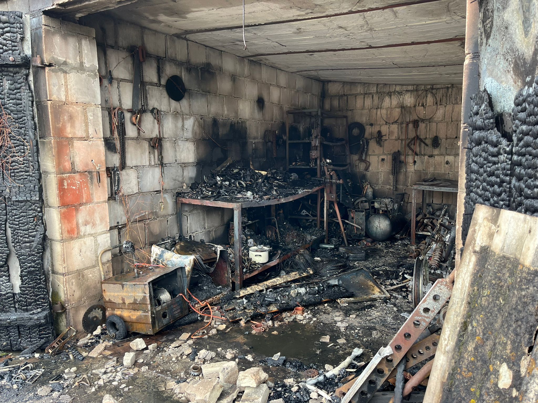 Zdjęcie przedstawia spaloną część garażową budynku, spalony sprzęt i wyposażenie garażu